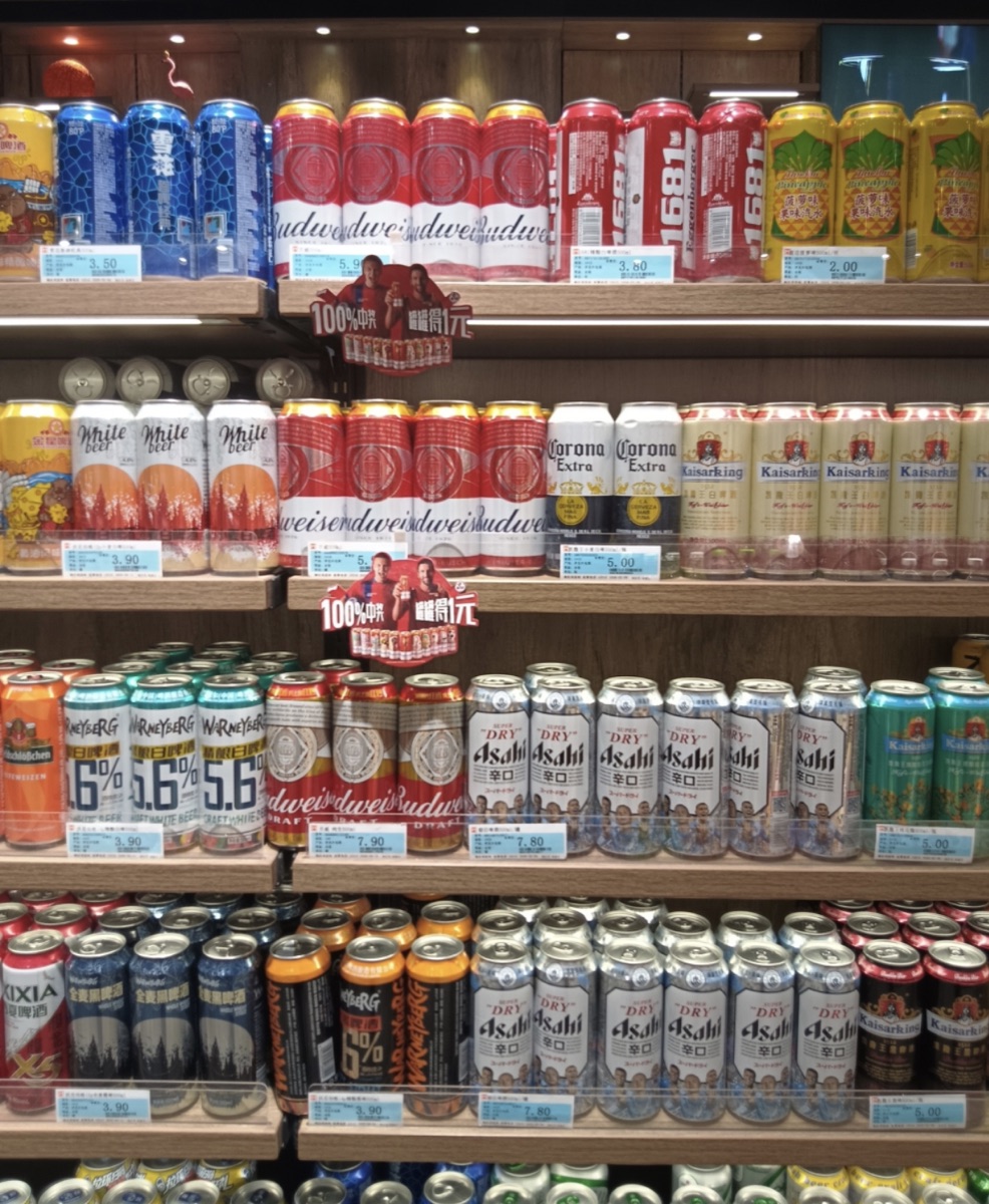 Multiple beer brands, prices, shelf positions, and promotional materials competing in one retail display