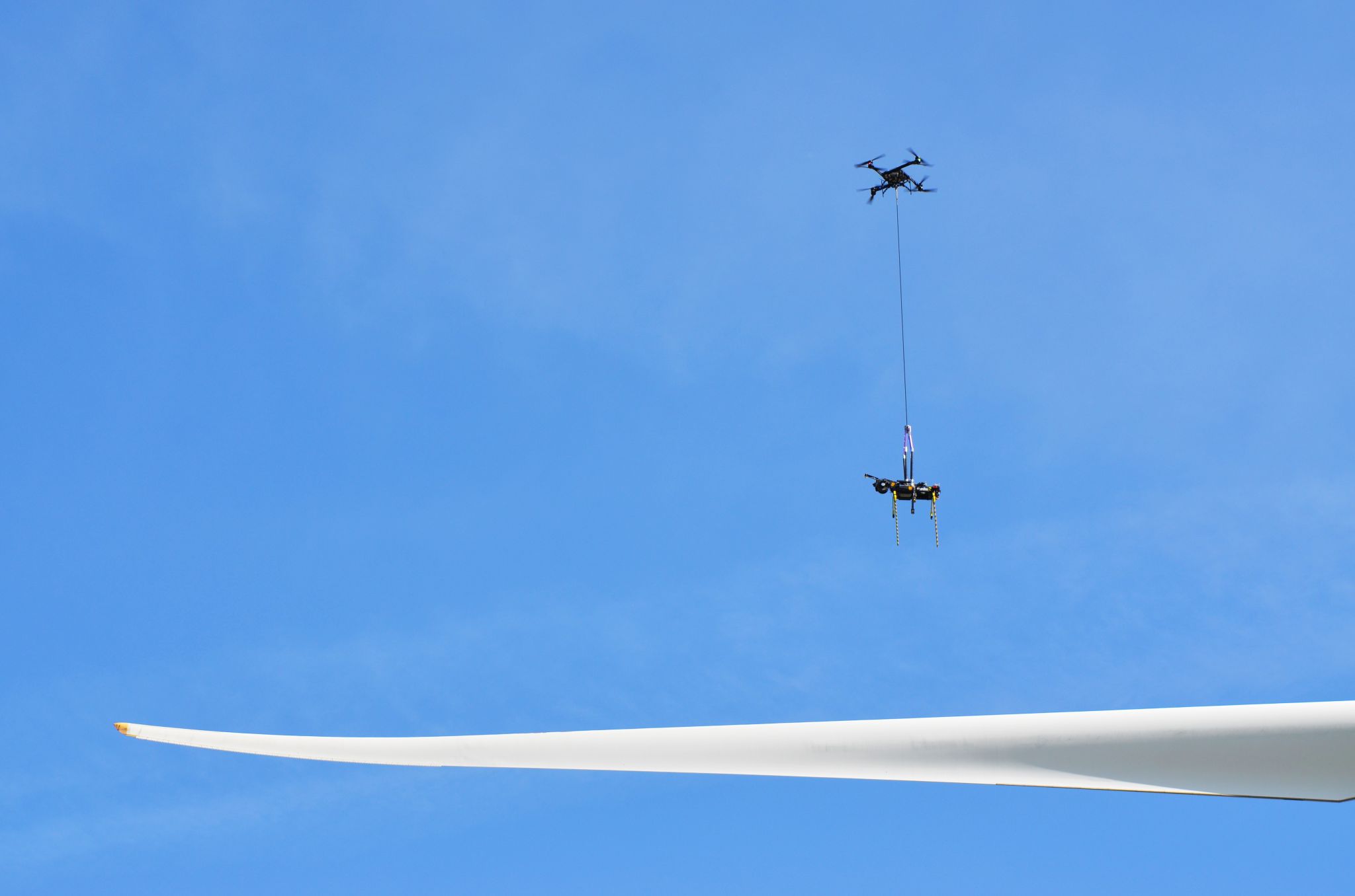 Heavy-lift drone lowering the SPARROW repair robot onto a wind turbine blade